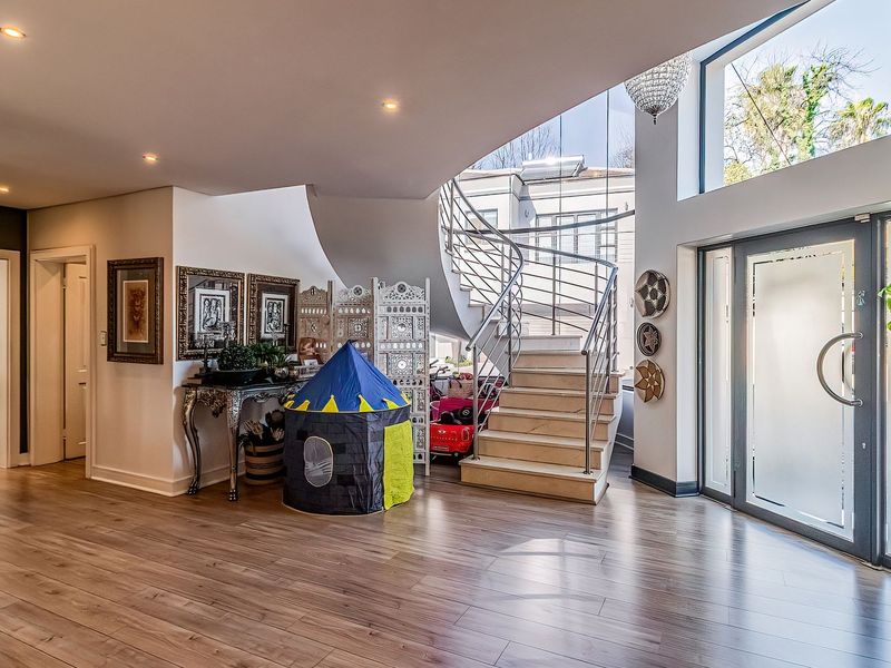 Spacious double-volume entrance hall featuring a modern spiral staircase with stainless steel balustrade, large glass entrance door, and high-quality laminate flooring.