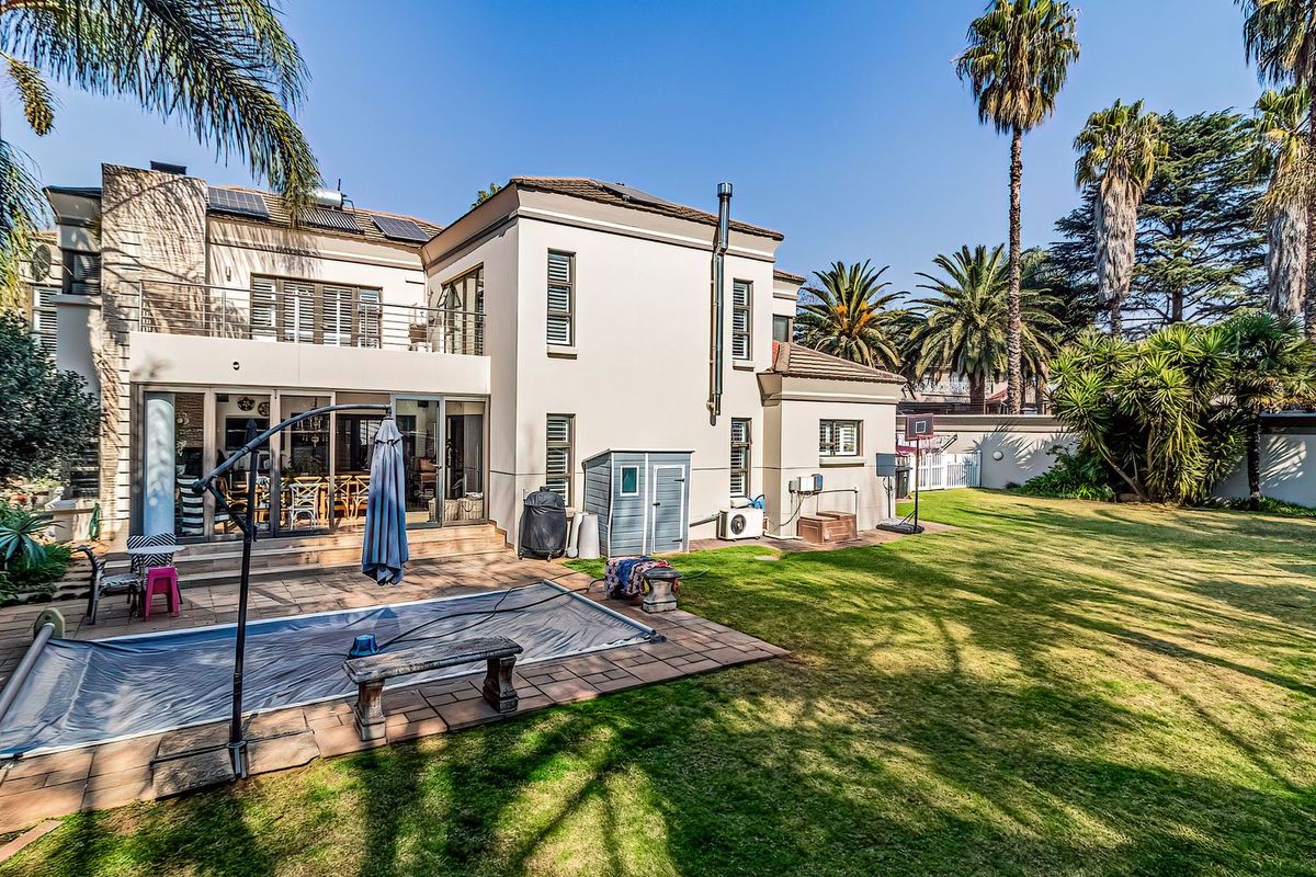 Spacious rear garden featuring a swimming pool with cover, paved patio area, and a two-story residence with balcony and solar panels.