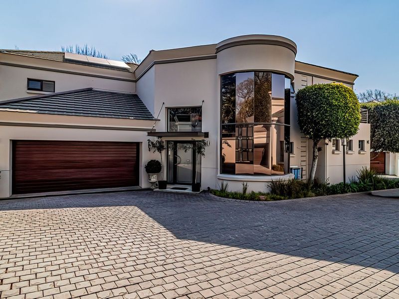 A modern cluster home featuring a paved driveway, double garage, and a striking curved glass architectural facade with solar panels on the roof.