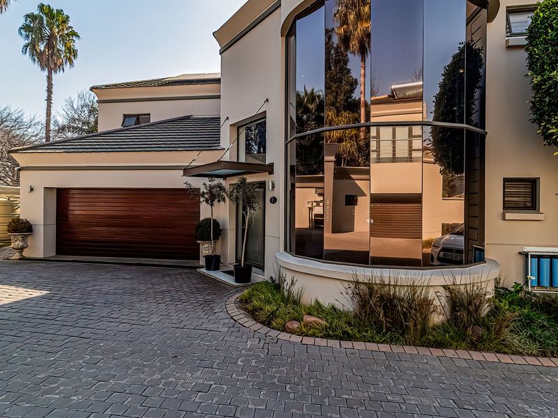 Modern cluster home exterior featuring a paved driveway, double garage, and a striking curved glass architectural element with integrated water storage and filtration systems.