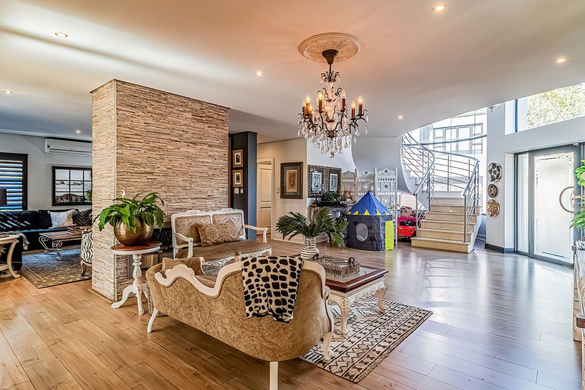 Spacious open-plan living area featuring a striking stone-clad feature wall, elegant chandelier, and a modern spiral staircase leading to the upper level.