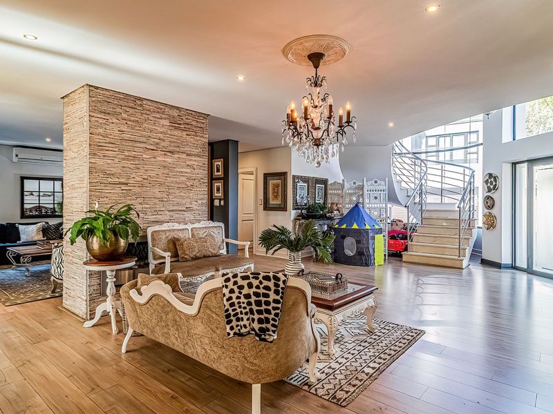 Spacious open-plan living area featuring a striking stone-clad feature wall, elegant chandelier, and a modern spiral staircase leading to the upper level.