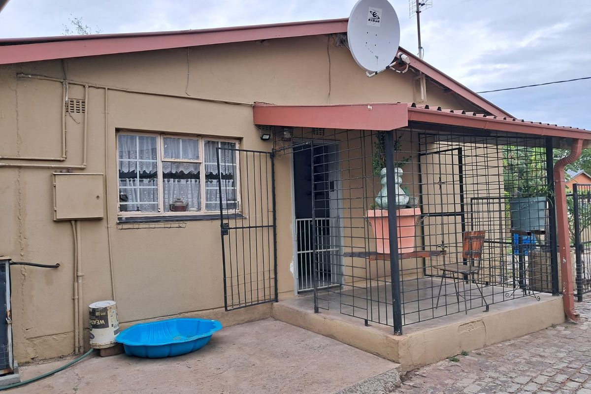 Rear exterior view of the house featuring a covered patio area with security gates and bars, concrete paving, and a satellite dish installation.