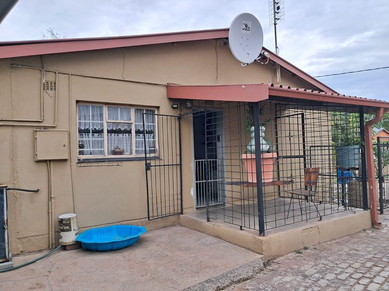 Rear exterior view of the house featuring a covered patio area with security gates and bars, concrete paving, and a satellite dish installation.