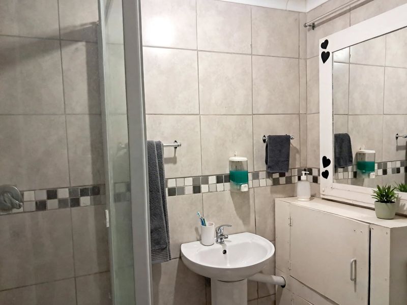 A functional bathroom featuring a pedestal basin, shower enclosure, and tiled walls with a decorative mosaic border.