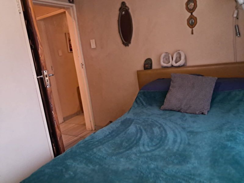 A bedroom featuring a built-in headboard and access to an adjacent hallway, showing signs of wear on the door frame and wall finishes.