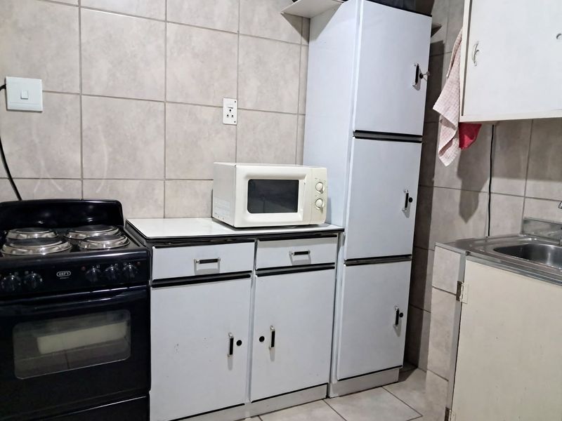 A compact kitchen area featuring built-in cabinetry, a stainless steel sink, tiled backsplash, and a freestanding electric stove and oven.