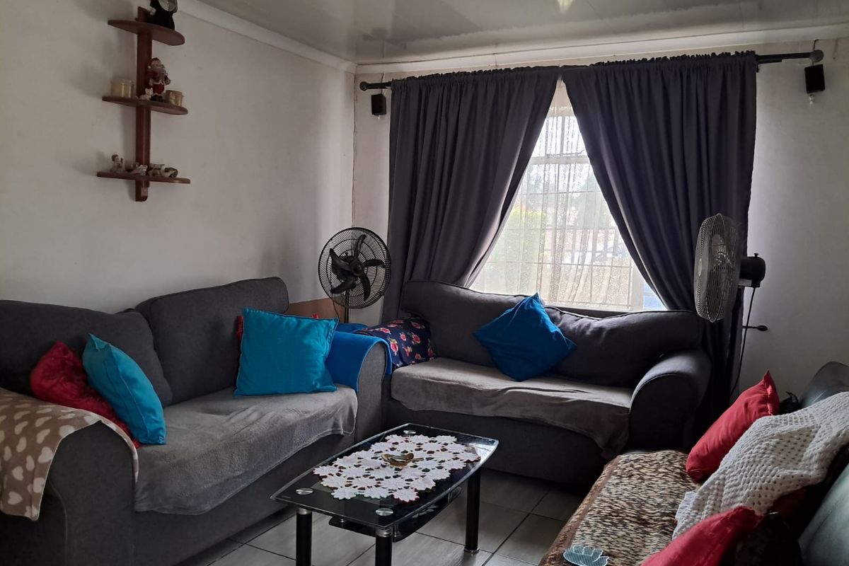 A living room featuring tiled flooring and a window with security bars, currently showing signs of wear including damaged ceiling panels.