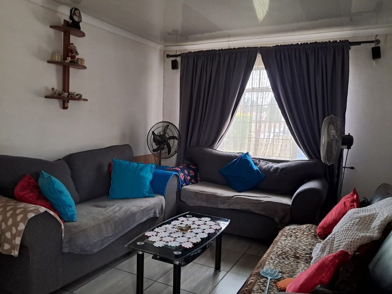 A living room featuring tiled flooring and a window with security bars, currently showing signs of wear including damaged ceiling panels.