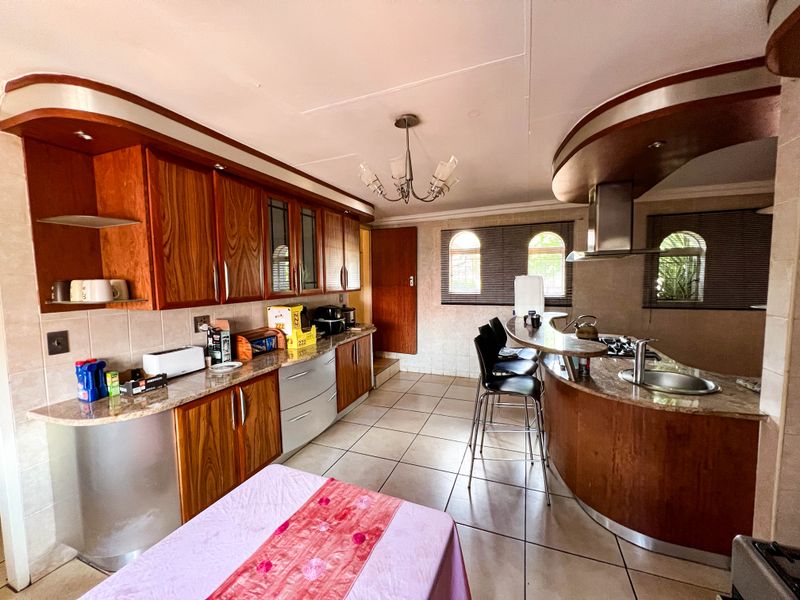 Spacious kitchen featuring wooden cabinetry, granite countertops, a curved breakfast bar, and a built-in hob with a stainless steel extractor fan.
