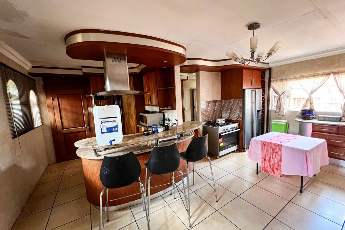 Spacious kitchen featuring a granite breakfast bar, wooden cabinetry, stainless steel extractor fan, and tiled flooring with a unique dropped ceiling design.