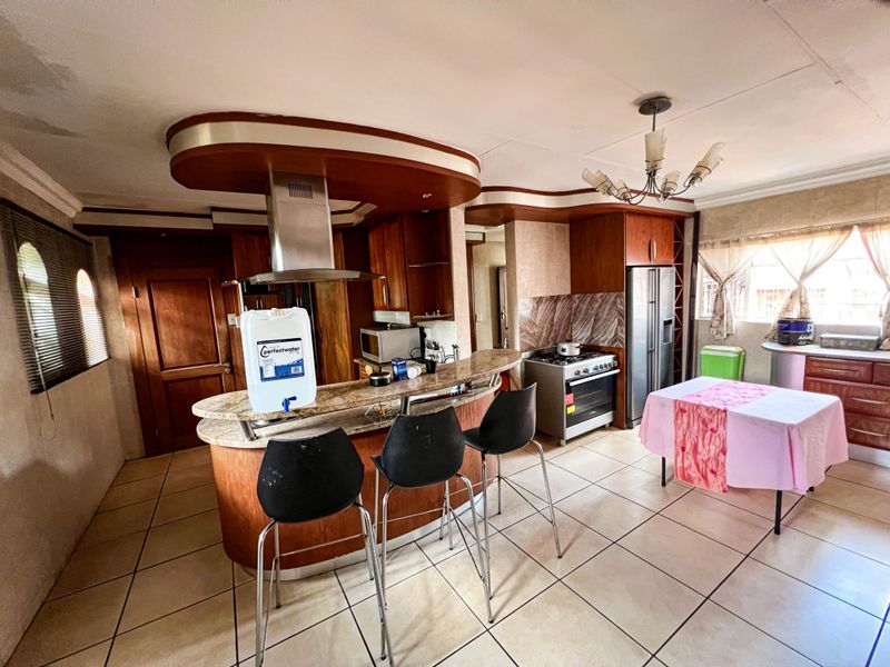 Spacious kitchen featuring a granite breakfast bar, wooden cabinetry, stainless steel extractor fan, and tiled flooring with a unique dropped ceiling design.