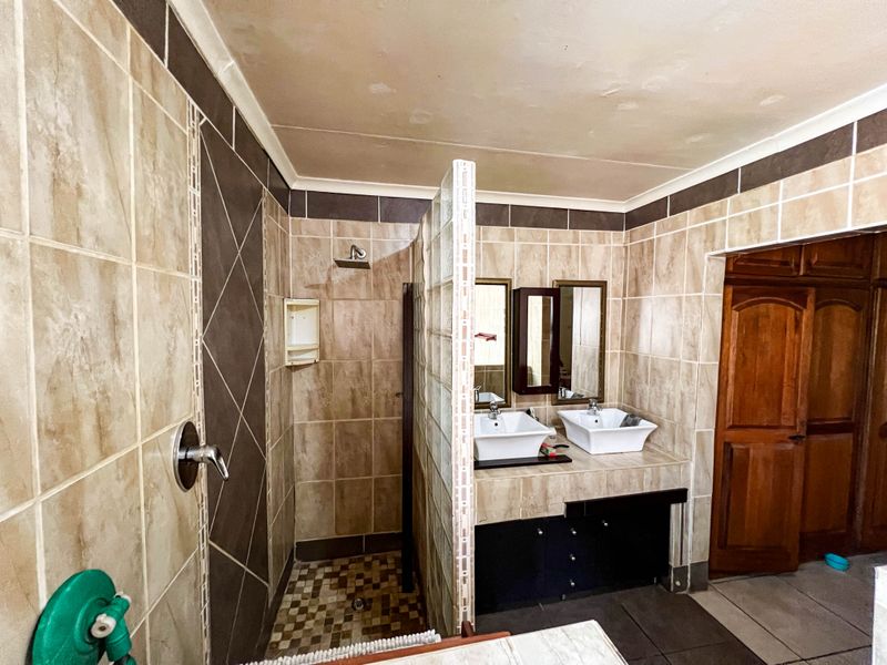 A functional bathroom featuring a double vanity with vessel sinks, a glass block partition, and a tiled walk-in shower area.
