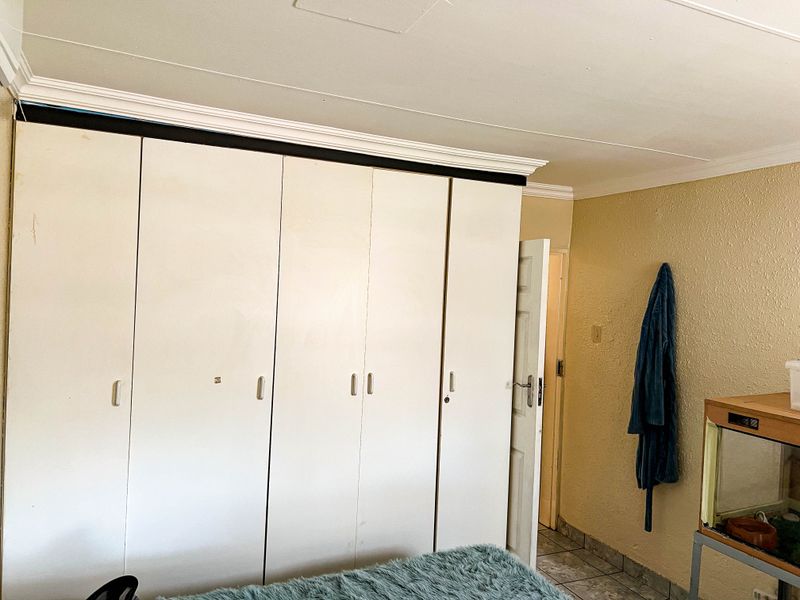 Bedroom featuring built-in cupboards with white doors, tiled flooring, and textured wall finishes.