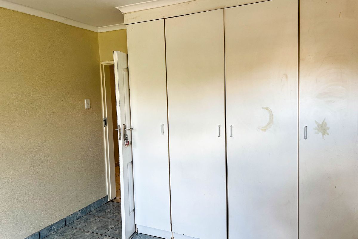 A bedroom featuring built-in cupboards and tiled flooring, requiring cosmetic updates to the wall finishes and cupboard surfaces.