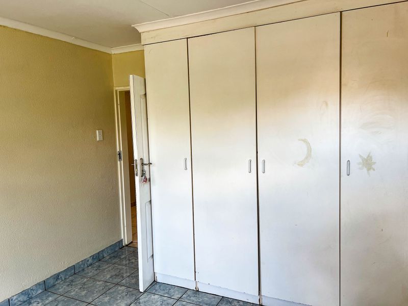 A bedroom featuring built-in cupboards and tiled flooring, requiring cosmetic updates to the wall finishes and cupboard surfaces.