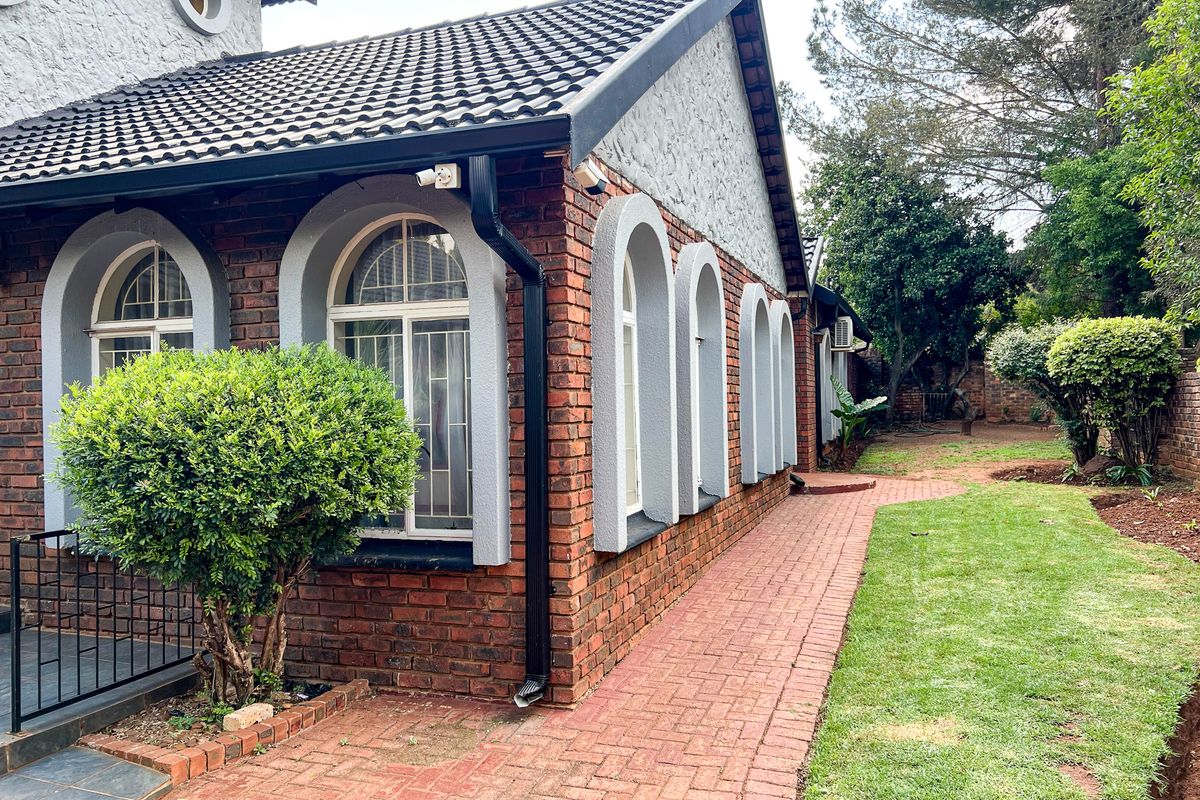 Rear exterior view of the house featuring face brick walls, arched window detailing, a paved walkway, and a well-maintained garden area.
