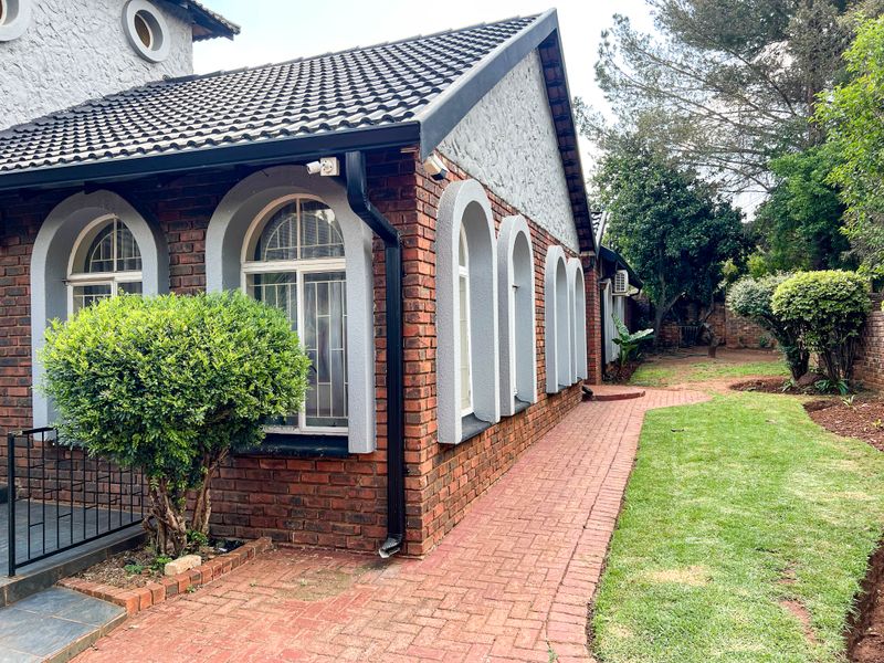 Rear exterior view of the house featuring face brick walls, arched window detailing, a paved walkway, and a well-maintained garden area.