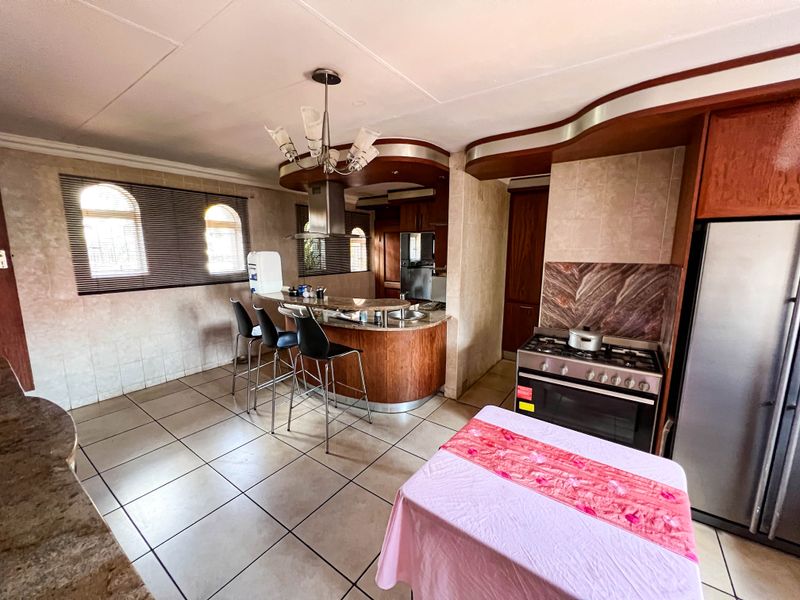 Kitchen featuring a curved breakfast bar, built-in oven with gas hob, stainless steel extractor fan, and tiled flooring throughout.