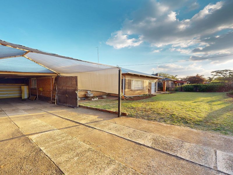 Rear view of the property featuring a concrete driveway, a shade cloth carport structure, and a spacious lawn area.