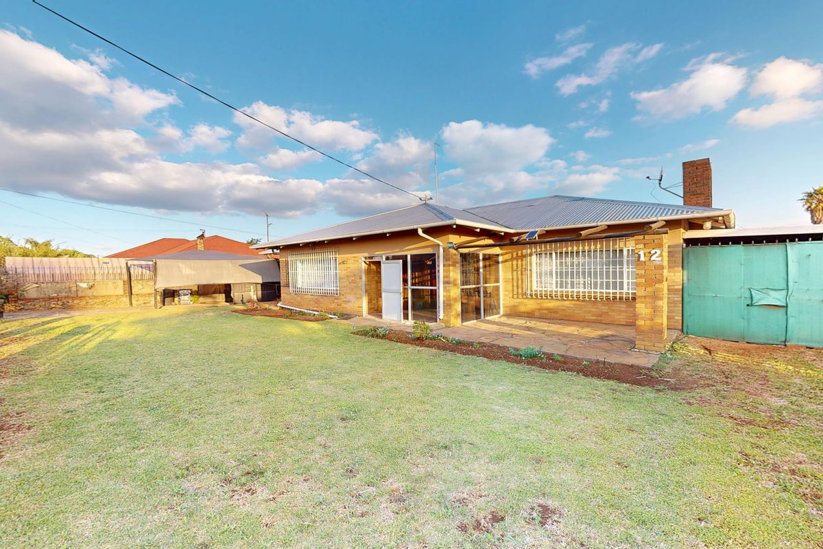 Rear view of a brick house featuring a stone patio, security bars on windows, and a spacious garden area.