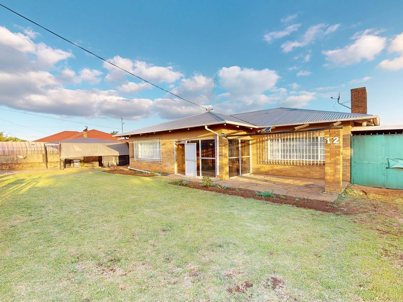 Rear view of a brick house featuring a stone patio, security bars on windows, and a spacious garden area.