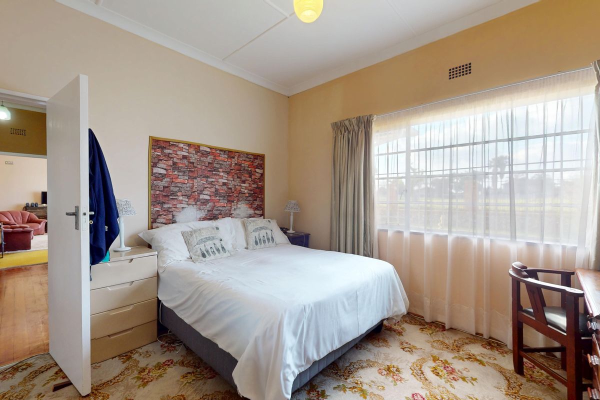 A bedroom featuring a large window, hardwood flooring, and a view into the adjacent living area.