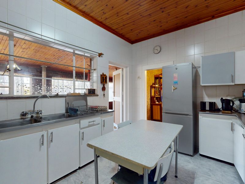 A functional kitchen featuring white cabinetry, tiled splashbacks, and a distinctive timber ceiling, offering a dated aesthetic ready for modernization.