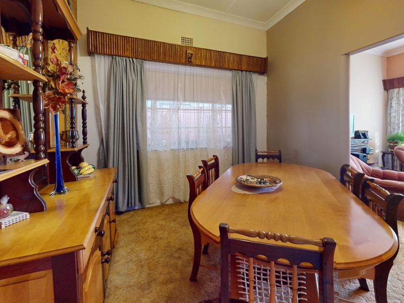 A traditional dining room featuring carpeted flooring, decorative window pelmets, and coved cornicing, connecting to an adjacent living area.