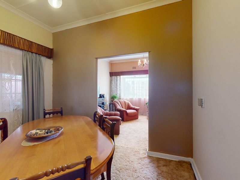 Dining room featuring carpet flooring and a wide opening leading into the adjacent living area, with neutral wall tones and classic window pelmets.