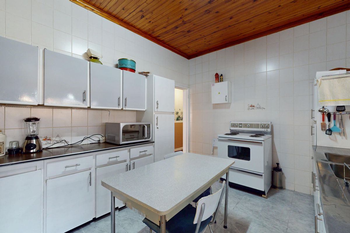 A functional kitchen featuring white cabinetry, tiled walls, a timber ceiling, and a freestanding stove, offering potential for modern renovation.
