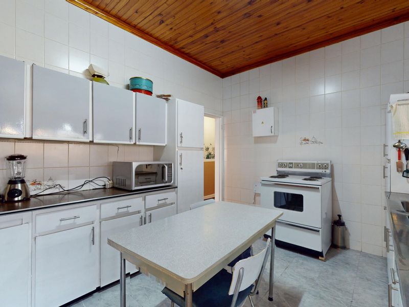 A functional kitchen featuring white cabinetry, tiled walls, a timber ceiling, and a freestanding stove, offering potential for modern renovation.