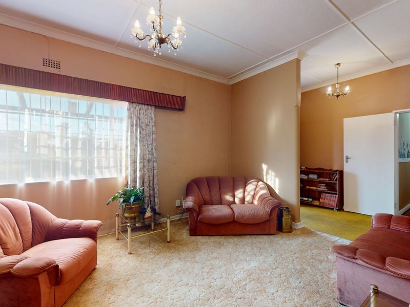 A dated living room featuring original ceiling coving, security bars on the window, and built-in shelving, offering potential for a modern renovation.