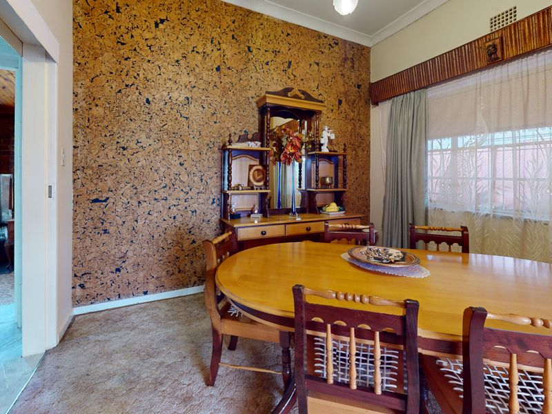 Dining room featuring a distinctive cork-clad feature wall, large window with pelmet, and carpeted flooring, offering potential for a modern update.