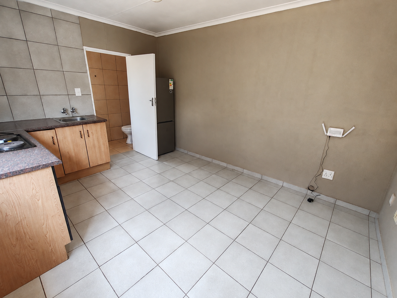 Open plan kitchen area featuring tiled flooring, built-in cabinetry with laminate countertops, and an adjacent bathroom access point.