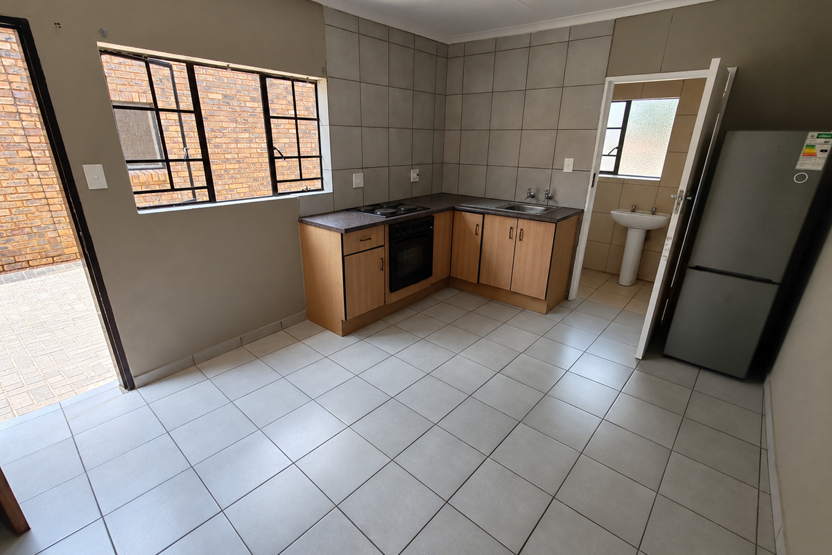 Functional kitchen featuring built-in cabinetry, oven, hob, and tiled finishes, with direct access to an outdoor area and adjacent utility space.