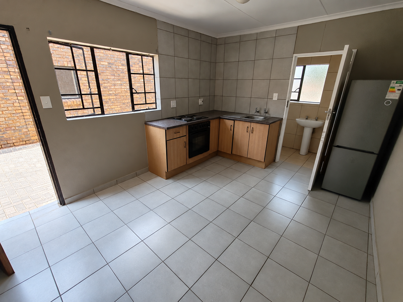 Functional kitchen featuring built-in cabinetry, oven, hob, and tiled finishes, with direct access to an outdoor area and adjacent utility space.