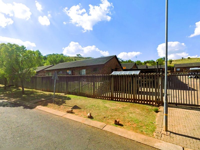 Street view of a townhouse complex featuring brick facades, tiled roofs, and secure perimeter fencing with a gated driveway entrance.