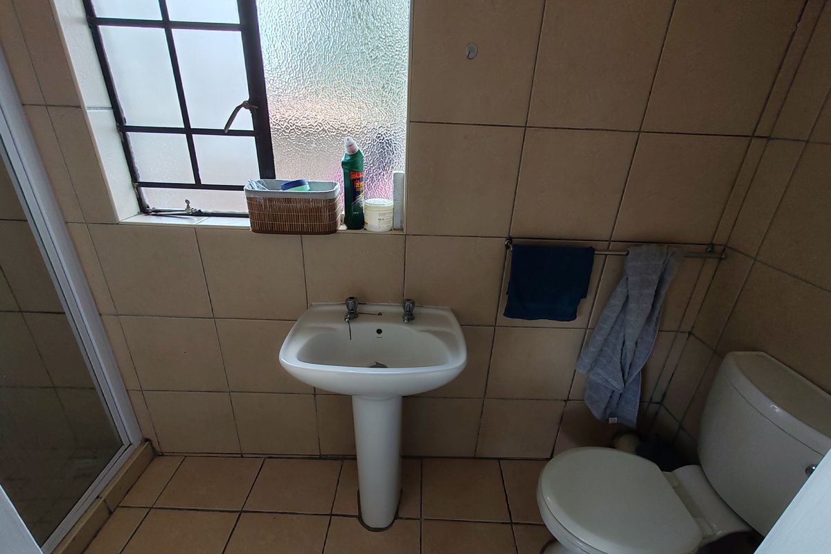 A functional bathroom featuring a pedestal basin, toilet, and shower enclosure with neutral wall and floor tiling.
