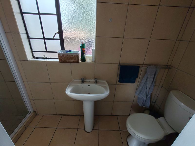 A functional bathroom featuring a pedestal basin, toilet, and shower enclosure with neutral wall and floor tiling.