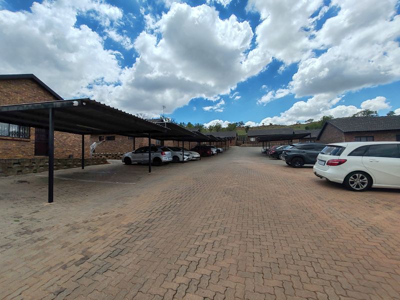 Exterior view of a townhouse complex featuring a paved driveway and covered carport parking bays with facebrick building exteriors.