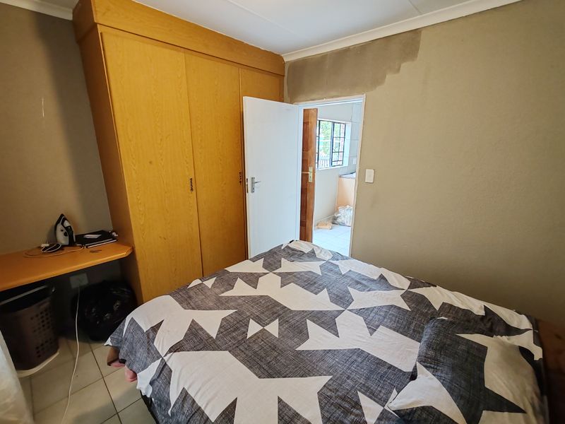 A bedroom featuring built-in wooden wardrobes and tiled flooring, currently requiring cosmetic attention to the wall finishes.