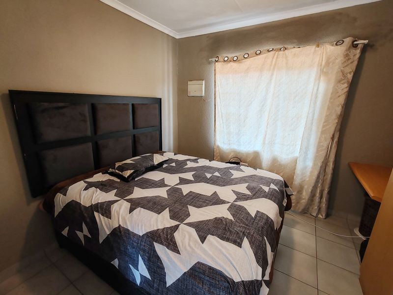 A bedroom featuring tiled flooring and a built-in desk, showing signs of wall staining and wear that would benefit from cosmetic updates.
