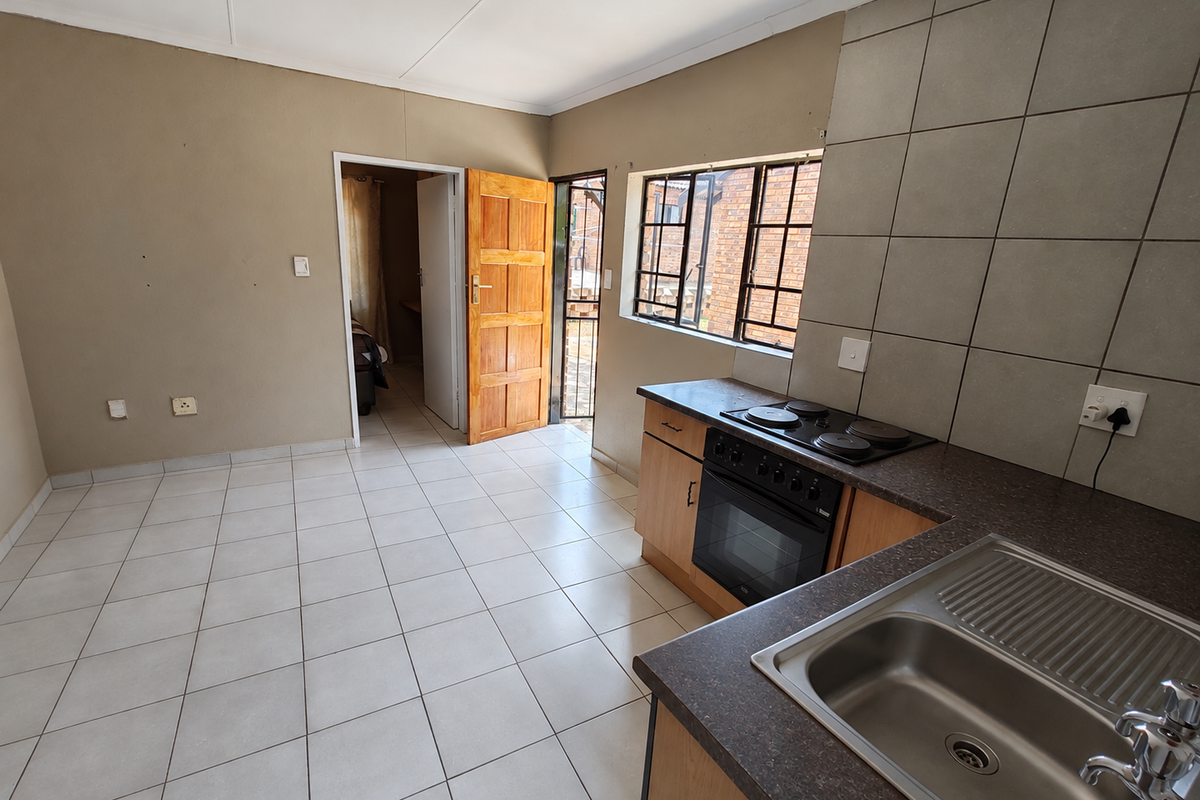 A functional, empty kitchen featuring built-in cabinetry, a stainless steel sink, and an electric stove, with direct access to an exterior security gate.