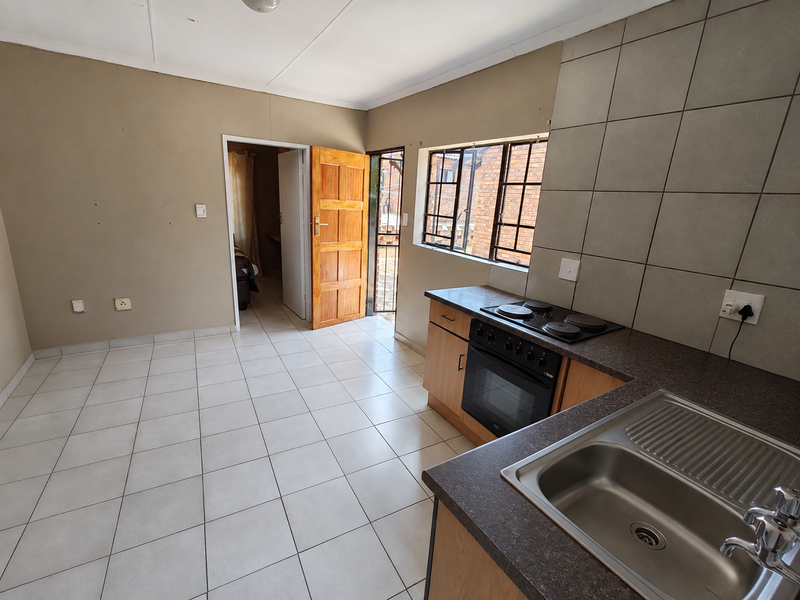 A functional, empty kitchen featuring built-in cabinetry, a stainless steel sink, and an electric stove, with direct access to an exterior security gate.