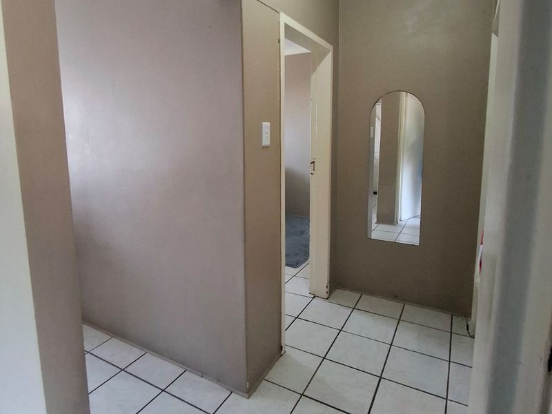 A vacant hallway featuring tiled flooring and a coved ceiling, providing access to adjacent rooms through an archway.