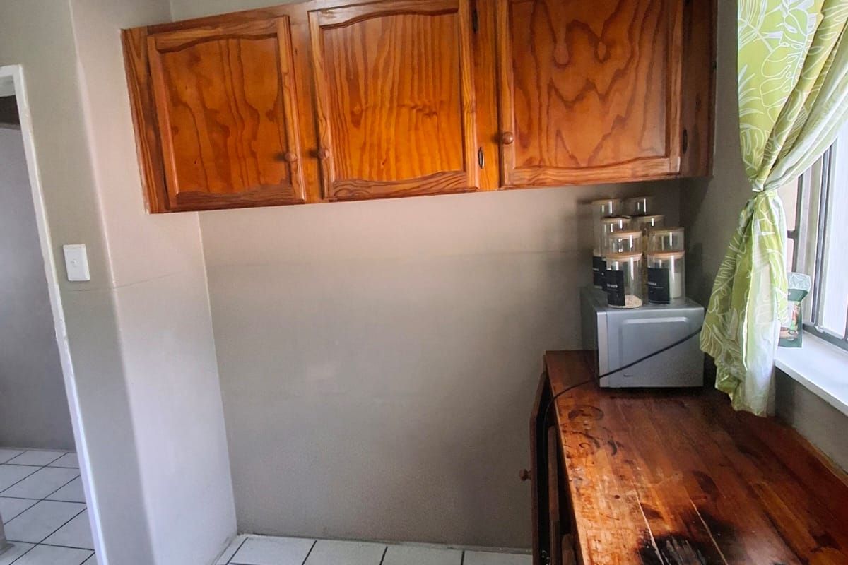 A kitchen area featuring wooden cabinetry and a worn wooden countertop, complemented by tiled flooring and neutral wall tones.