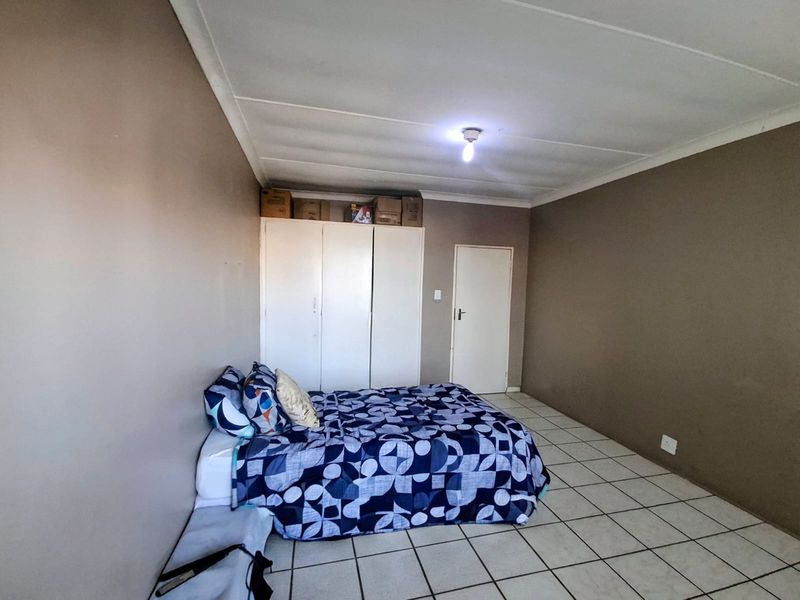 A functional bedroom featuring built-in cupboards, tiled flooring, and neutral wall tones, offering a blank canvas for personalization.
