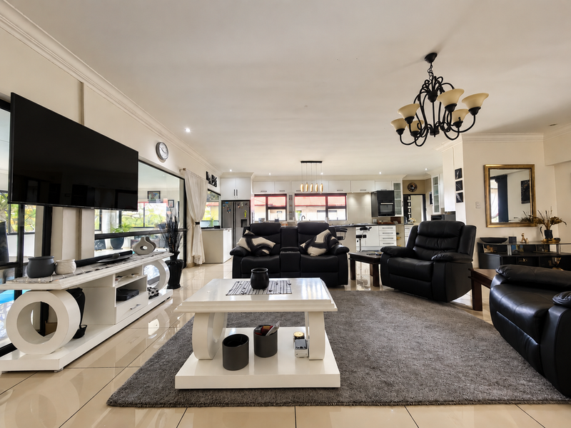 Spacious open-plan living area featuring tiled floors, modern kitchen cabinetry, and a central island, seamlessly connecting to the outdoor space through sliding glass doors.