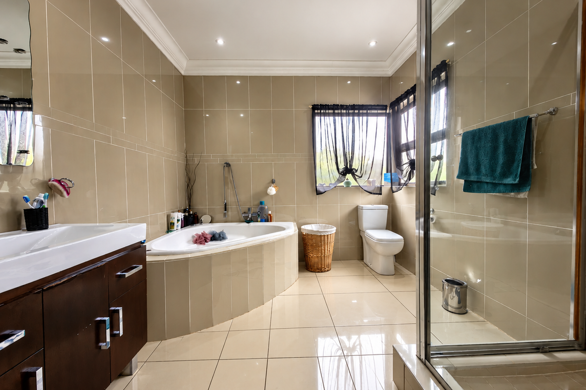 A spacious bathroom featuring a built-in vanity, a corner drop-in bathtub, a separate glass-enclosed shower, and neutral floor-to-ceiling wall tiles.